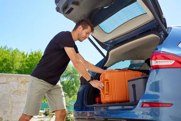 Güneşli bir günde turuncu bavulu bagaja yükleyen adam. Yaz seyahatine, tatile ya da bavulla yolculuğa hazırlanma kavramı