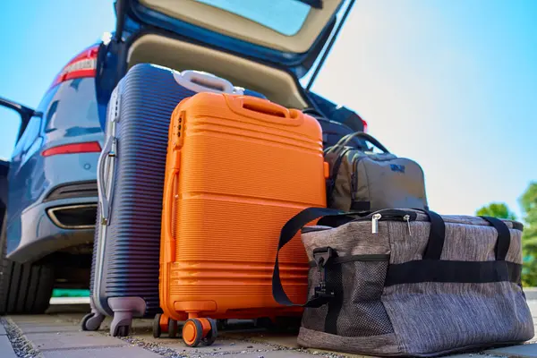 Bagajlar ve bavullar açık araba bagajının önünde, banliyö evinin yanındaki kaldırımda duruyor. Yolculuk ya da taşınmadan önce araca yüklemeye hazırız. Taşınma ya da yolculuk kavramı