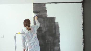 Koruyucu takım elbiseli, beyaz pantolonlu, siyah baskılı, yenileme sırasında tekerlekli paten kullanan bir kadın. İç duvarı boyayan kadın işçi. Evde tadilat ve iyileştirme kavramı