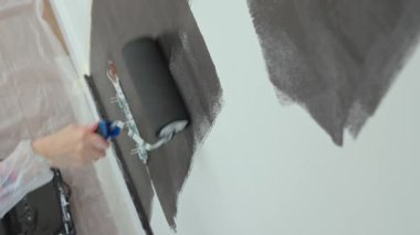 Ev tadilatı sırasında elektrik prizlerinin yakınındaki duvarı siyaha boyamak için silindir kullanan kişinin ayrıntılı görüntüsü