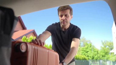 Turuncu bavulu açık bir bagaja koyup güneşli bir günde yolculuğa ya da tatile hazırlanan bir adam. Gezginlerin bagajlarını arabaya yüklediğini gördüm. Seyahat ya da hafta sonu yolculuk konsepti