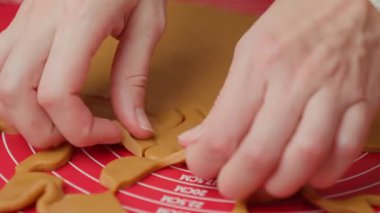 Kırmızı hasırda zencefilli ekmek hamuru şekillendirmek için kurabiye keskisi kullanan şenlikli kazaklı bir kadın. Ev mutfağında geleneksel Noel kurabiyeleri pişiriyorum.