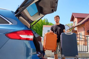Tuğla evin önünde bagajı açık iki bavul tutan adam. Erkek sürücü bagajı araca yüklemeye hazırlanıyor. Taşınma veya yeni eve taşınma kavramı