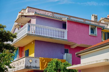 Kırmızı, mor, sarı ve mavi duvarları ve yemyeşil ve üzümlerle çevrili balkonları olan renkli bir apartman. Kıyı kasabasında ikamet yeri.