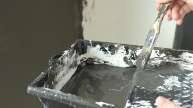 Kadın cam kenarındaki duvarı fırça ve boya tepsisiyle boyuyor, koruyucu takım elbise giyiyor. Ev yenileme, DIY dekorasyon ve duvar boyama kavramı