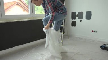 Modern odada resim projesine hazırlanan kadın, duvarda boya örnekleriyle koruyucu kılıf takıyor. DIY ev yenileme kavramı, yeniden dekorasyon ve iç iyileştirme planlama
