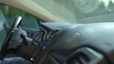 Adam arabanın ön panelini mikrofiber bez ve sprey şişeyle temizliyor. Otomobil bakımı, araba dezenfeksiyonu ve araba hijyeni kavramı