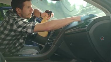 Adam arabanın ön panelini mikrofiber bez ve sprey şişeyle temizliyor. Otomobil bakımı, araba dezenfeksiyonu ve araba hijyeni kavramı