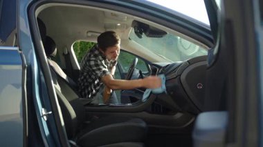 Adam arabanın ön panelini mikrofiber bez ve sprey şişeyle temizliyor. Otomobil bakımı, araba dezenfeksiyonu ve araba hijyeni kavramı