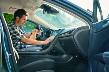 Adam arabanın ön panelini mikrofiber bez ve sprey şişeyle temizliyor. Otomobil bakımı, araba dezenfeksiyonu ve araba hijyeni kavramı