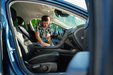 Adam arabanın içini mikrofiber bez ve spreyle temizliyor. Otomobil bakımı, dezenfeksiyon ve araç hijyeni kavramı