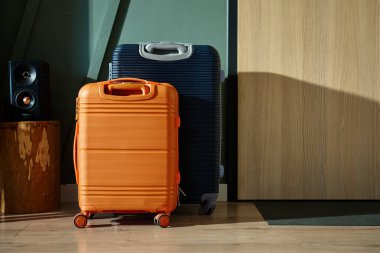 İki modern bavul, turuncu ve lacivert, sabah ışığında giriş kapısının yanında durun. Oturma odasındaki bavullar tatil için hazır. Seyahat hazırlığı kavramı