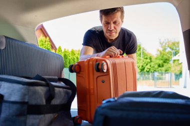 Turuncu bavulu açık bir bagaja koyup güneşli bir günde yolculuğa ya da tatile hazırlanan bir adam. Gezginlerin bagajlarını arabaya yüklediğini gördüm. Seyahat ya da hafta sonu yolculuk konsepti