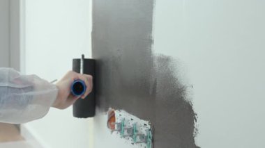 Ev tadilatı sırasında elektrik prizlerinin yakınındaki duvarı siyaha boyamak için silindir kullanan kişinin ayrıntılı görüntüsü