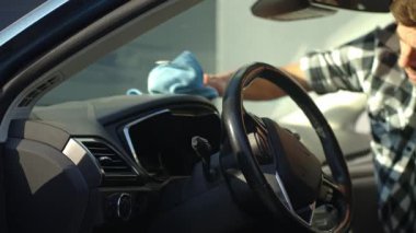 Adam arabanın ön panelini mikrofiber bez ve sprey şişeyle temizliyor. Otomobil bakımı, araba dezenfeksiyonu ve araba hijyeni kavramı