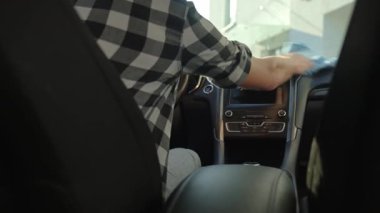 Adam arabanın içinde otururken arabanın ön panelini mikrofiber bezle siliyor. İç temizlik, araç bakımı ve araba bakımı kavramı