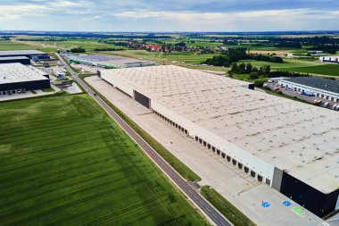 Yükleme limanları ve yeşil tarlalarla çevrili park edilmiş kamyonları olan büyük, modern bir depo. Sanayi lojistik merkezi. Tedarik zinciri sisteminde dağıtım, nakliye ve depolama için altyapı
