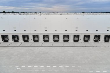 Lojistik deposunun dış tarafındaki yükleme platformlarının havadan görüntüsü. Dağıtım merkezinde kamyon ambarları ve kapalı yükleme kapıları. Nakliye işlemleri için ticari altyapı