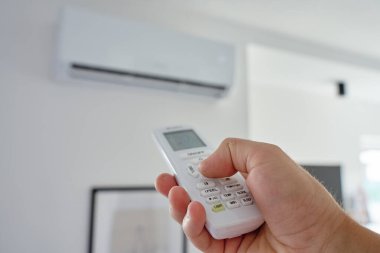 Modern odadaki duvara monte edilmiş klimanın ısısını ayarlamak için uzaktan kumandayı kullan. Ev konforu için sıcaklık kontrolü kavramı