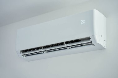 Parlak odadaki beyaz duvara monte edilmiş modern klima ünitesinin yakın görüntüsü. Ev soğutma teknolojisi, iklim kontrolü, enerji verimliliği ve sıcak havada konfor