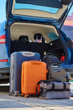 Bagajlar ve bavullar açık araba bagajının önünde, banliyö evinin yanındaki kaldırımda duruyor. Yolculuk ya da taşınmadan önce araca yüklemeye hazırız. Taşınma ya da yolculuk kavramı