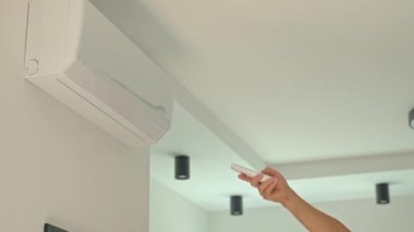 Uzaktan kumandayı tutan ve evdeki duvara monte edilmiş klimanın ısısını ayarlayan yakın plan. Sıcak havalarda serinleme ve iklim kontrolü kavramı