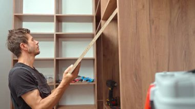 Evdeki ahşap gardırobu, aletleri kullanarak ve büyük ahşap paneli tutarak yapan adam. DIY mobilya montajı, ev geliştirme ve yenileme işi kavramı