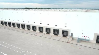 Lojistik deposunun dış tarafındaki yükleme platformlarının havadan görüntüsü. Dağıtım merkezinde kamyon ambarları ve kapalı yükleme kapıları. Nakliye işlemleri için ticari altyapı