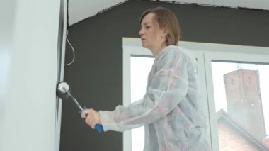 Koruyucu takım elbiseli bir kadın yenileme sırasında siyah baskı ile beyaz duvar boyuyor. İç duvarı boyayan kadın işçi. Evde tadilat ve iyileştirme kavramı