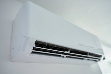 Parlak odadaki beyaz duvara monte edilmiş modern klima ünitesinin yakın görüntüsü. Ev soğutma teknolojisi, iklim kontrolü, enerji verimliliği ve sıcak havada konfor