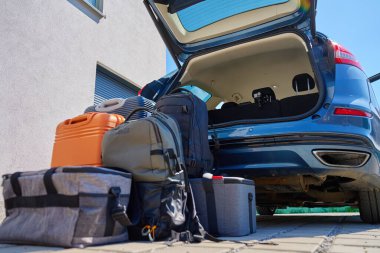 Bagajlar ve bavullar açık araba bagajının önünde, banliyö evinin yanındaki kaldırımda duruyor. Yolculuk ya da taşınmadan önce araca yüklemeye hazırız. Taşınma ya da yolculuk kavramı