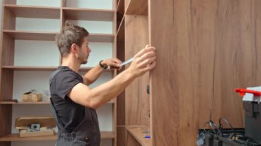 Mobilya montajı sırasında tahta dolabı mezurayla ölçen, arka planda aletleri ve vidaları olan bir adamın yakın çekimi. Ev yenileme ve DIY mobilya projesi kavramı
