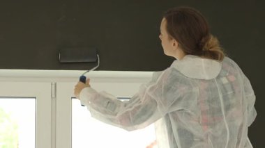 Kadın iç duvarı siyah boyayla boyuyor. Paten fırçası kullanıyor, koruyucu giysisi var. Ev yenileme, yeniden dekorasyon ve modern yaşam alanındaki iç iyileştirme kavramı