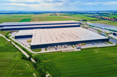 Yükleme limanları ve yeşil tarlalarla çevrili park edilmiş kamyonları olan büyük, modern bir depo. Sanayi lojistik merkezi. Tedarik zinciri sisteminde dağıtım, nakliye ve depolama için altyapı