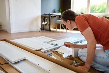 Kadın evde yeni bir yatak kuruyor, yerde oturuyor ve kullanma kılavuzunu okuyor. DIY ev mobilyaları montajı, ev geliştirme ve modern iç mekanda kendi kendine kurulum süreci kavramı