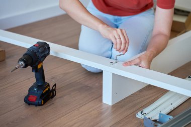 Ahşap zeminde, ingiliz anahtarı ve matkapla döşeme için yatak çerçevesi monte eden kadın. DIY mobilya montajı ve ev geliştirme