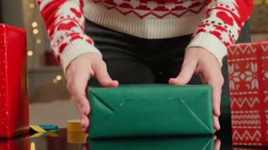 Noel hediyelerini kırmızı ve yeşil kağıda saran kadın elleri. Şenlikli kazaklı kadın kış tatili için hediyeler hazırlıyor. Noel ve Yeni Yıl Aile Gelenekleri