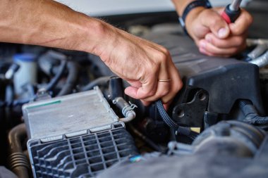 Kaputun altında araba motorunu tamir etmek için mandal kullanan tamircinin yakın görüntüsü. Otomobil servisi, araba bakımı ve teknik onarım