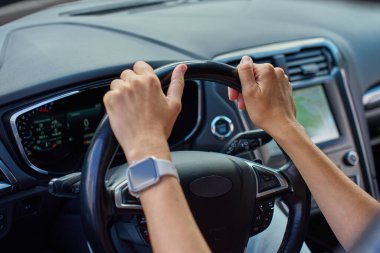 Arka planda gösterge paneli olan modern arabanın içinde direksiyonu tutan ellerin yakın çekimi. Araba kullanan kadın.