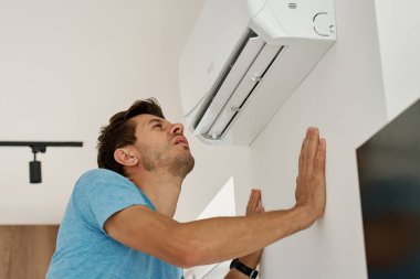 Adam klimanın yanında duruyor ve sıcak bir günde serin havanın tadını çıkarıyor. Ev iklimi kontrolü ve yazın serinleme kavramı