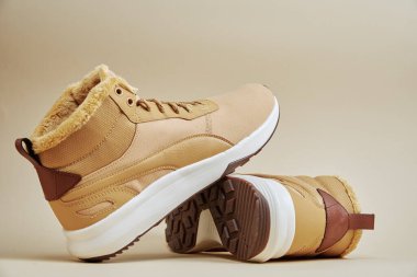 Bir çift şık kış botu, kürk astarlı ve bej arka planda lastik tabanlı. Soğuk hava için sıcak ayakkabılar