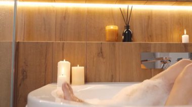 Küvette köpük ve sicak isik dolu kadin bacaklari. Banyoda mumlarla dinlenen bir kadın. Sağlık, rahatlama ve kendine dikkat etme kavramı.