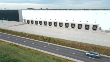 Lojistik deposunun dış tarafındaki yükleme platformlarının havadan görüntüsü. Dağıtım merkezinde kamyon ambarları ve kapalı yükleme kapıları. Nakliye işlemleri için ticari altyapı