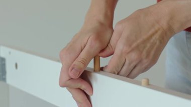 Kadın elleri toplantı sırasında beyaz mobilya tahtasına tahta döşeme takıyor. Kadınlar mobilya parçalarını tahta çivilerle birleştiriyor.