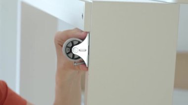 Beyaz yatak çerçevesine tekerlekleri vidalamak için kablosuz matkap kullanan bir kadın. Yeni dairede mobilya montajı yapan bir kadın. DIY ev yenileme ve taşınma konseptinden sonra ev organizasyonu