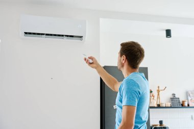 Modern iç mekanlarda duvarlara monte edilmiş klima ısısını ayarlamak için uzaktan kumanda kullanan bir adam. Sıcak yaz mevsiminde evde serinleme ve kapalı iklim kontrolü kavramı