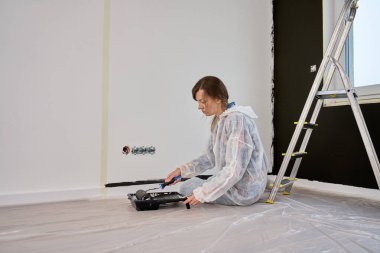 Koruyucu takım elbiseli, beyaz pantolonlu, siyah baskılı, yenileme sırasında tekerlekli paten kullanan bir kadın. İç duvarı boyayan kadın işçi. Evde tadilat ve iyileştirme kavramı