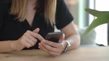 Masada oturan ve modern akıllı telefon kullanan bir kadının yakın çekimi. Kadın eli cep telefonu tutuyor, sosyal medyada geziniyor veya evde mesajlaşıyor