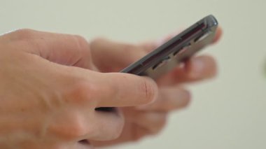 Masada oturan ve modern akıllı telefon kullanan bir kadının yakın çekimi. Kadın eli cep telefonu tutuyor, sosyal medyada geziniyor veya evde mesajlaşıyor