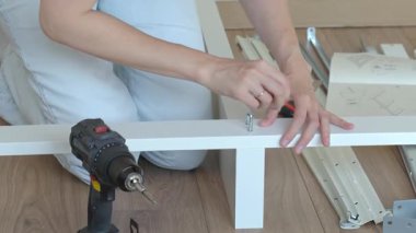 Ahşap zeminde, ingiliz anahtarı ve matkapla döşeme için yatak çerçevesi monte eden kadın. DIY mobilya montajı ve ev geliştirme